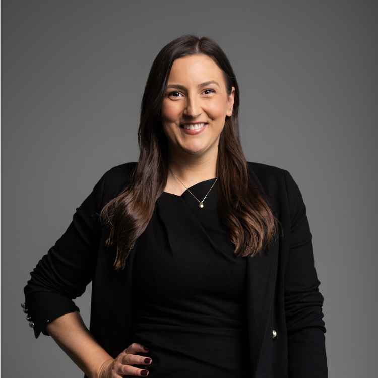 Amy Caldow headshot on a grey background in a black blazer.