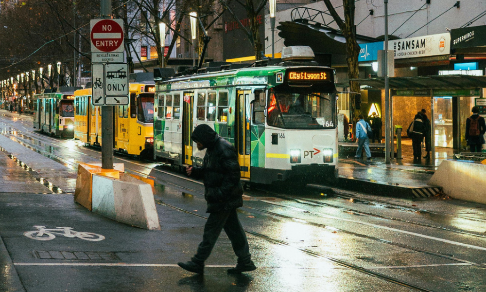 Pedestrian crossing tram tracks amid city traffic and wet road conditions